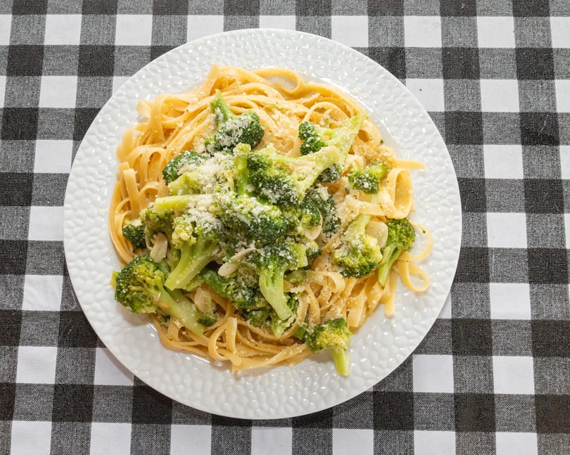 Fettuccine pasta with broccoli florets and grated cheese on a white plate, on a black and white checkered tablecloth.