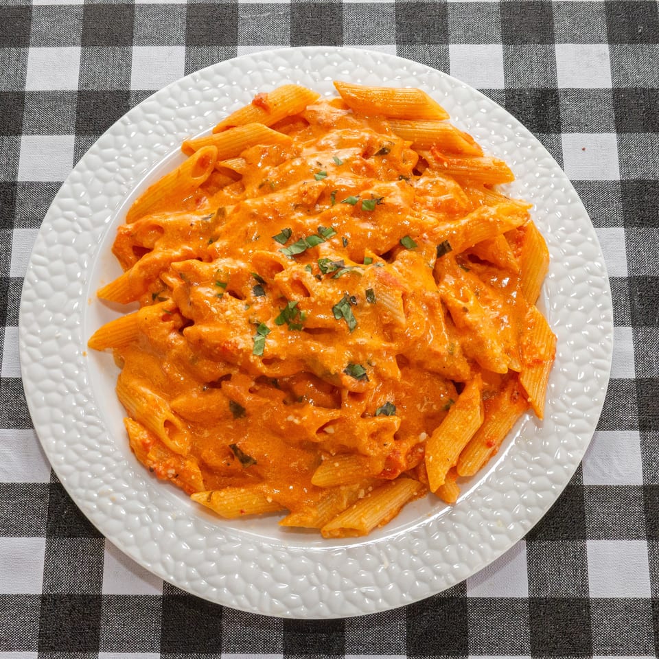 Penne pasta in a creamy tomato sauce, garnished with fresh herbs, on a white plate.