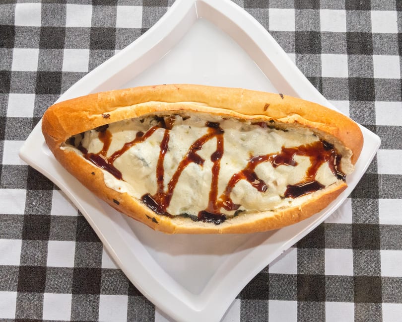 A long, golden-brown bread filled with creamy white cheese and drizzled with dark sauce on a white plate.