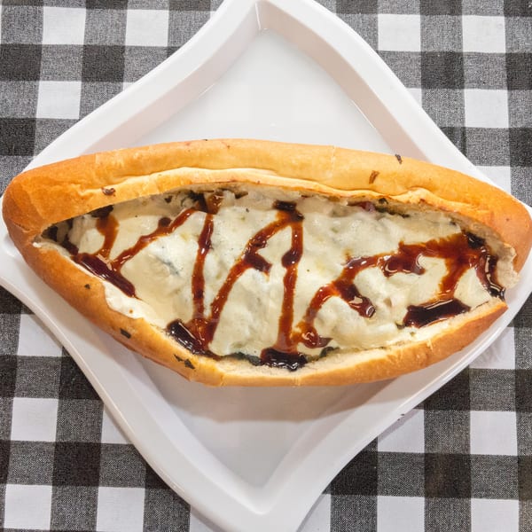 A long, golden-brown bread filled with melted cheese and drizzled with a dark sauce on a white plate.