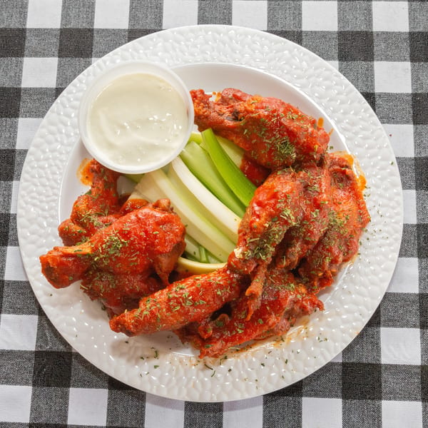 Spicy buffalo wings with celery sticks and a side of ranch dressing on a white plate.