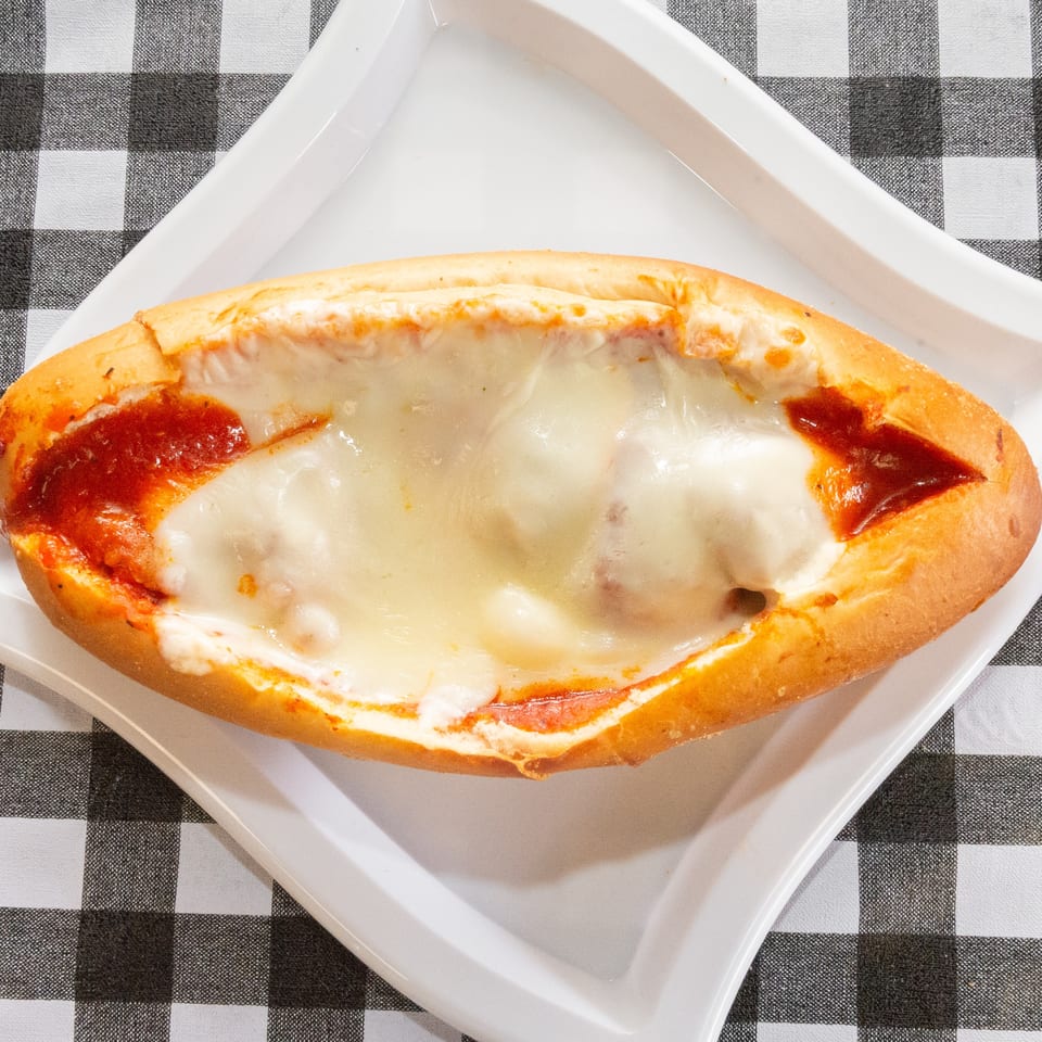Meatball sub with melted mozzarella cheese and marinara sauce on a white plate over a checkered tablecloth.