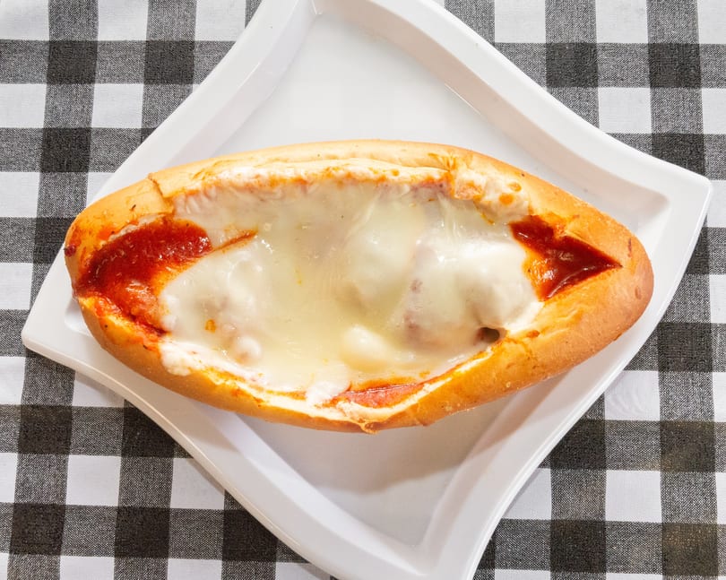 Meatball sub with melted mozzarella cheese and marinara sauce on a white plate over a checkered tablecloth.