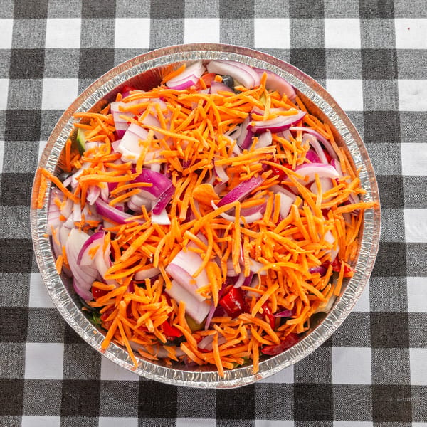 A foil container filled with shredded carrots and sliced red onions on a black and white checkered tablecloth.