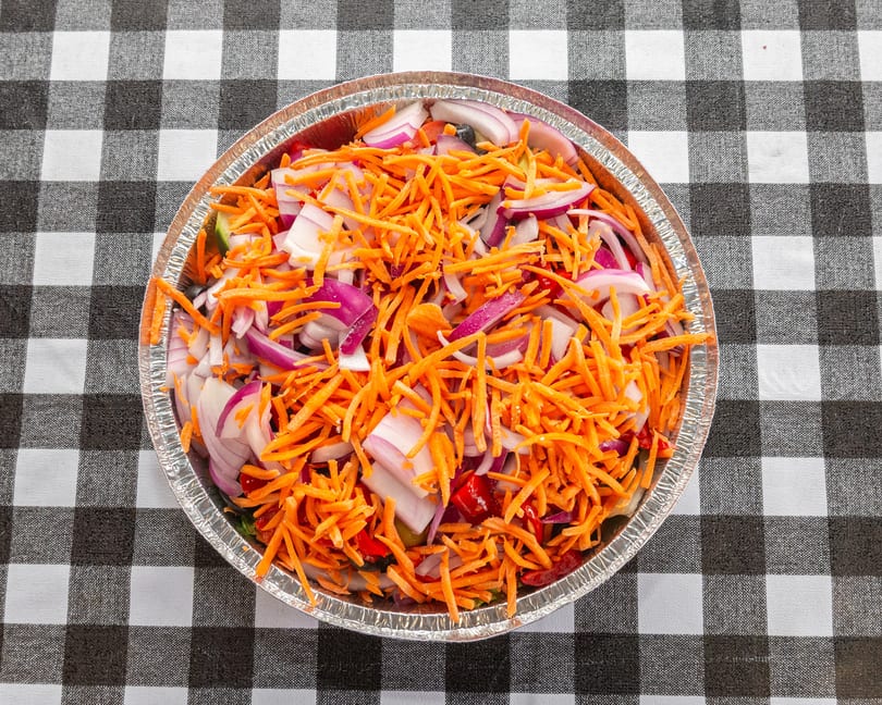 A foil container filled with shredded carrots and sliced red onions on a black and white checkered tablecloth.