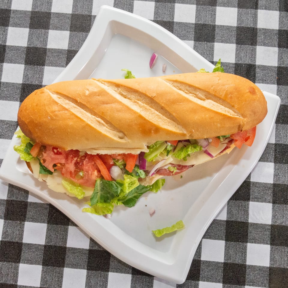 A large submarine sandwich with lettuce, tomato, onion, cheese, and deli meat on a white plate.