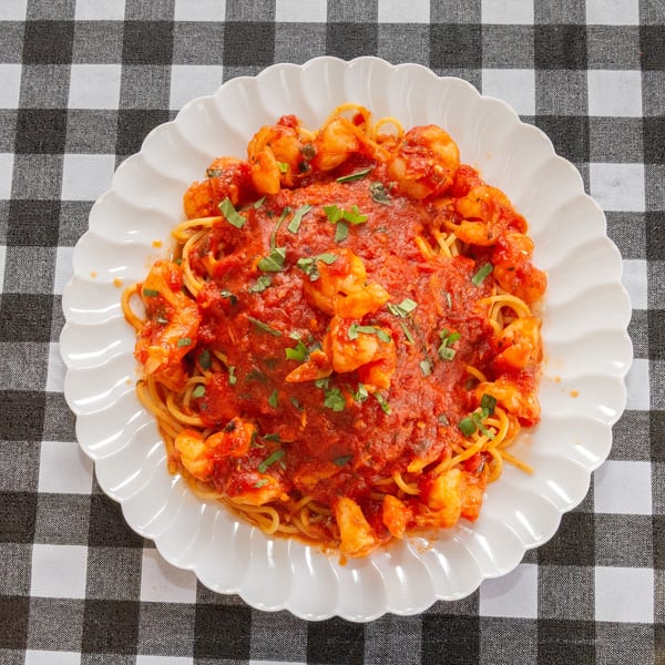 Spaghetti with shrimp and red sauce, garnished with basil, on a white plate over a checkered tablecloth.