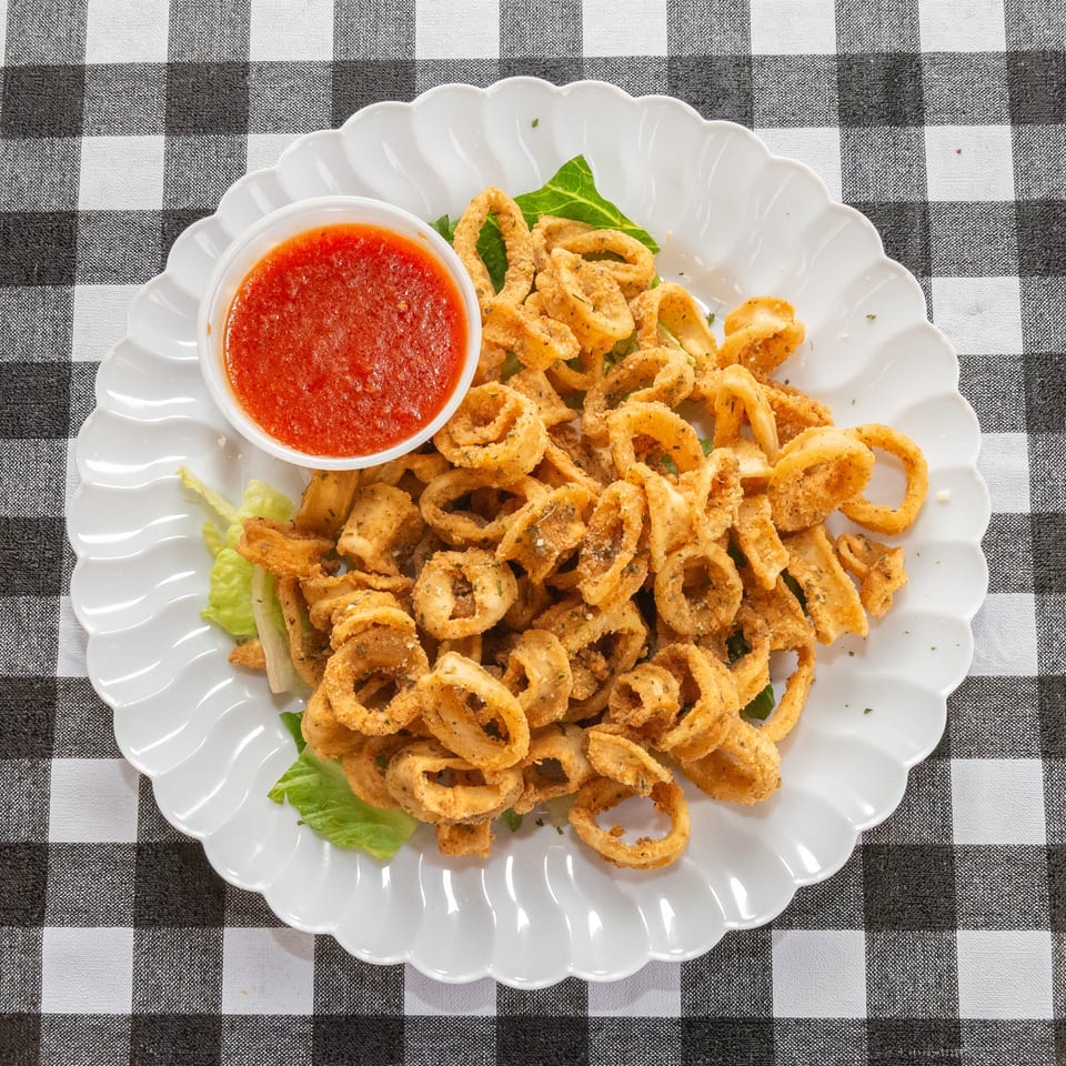Crispy fried calamari rings with a side of red marinara sauce on a white scalloped plate.