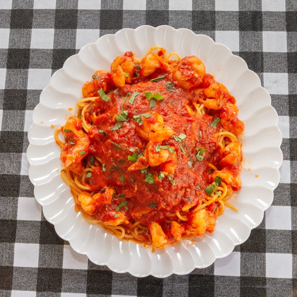 Spaghetti with shrimp and red sauce, garnished with basil, on a white plate over a checkered tablecloth.